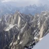 A breathtaking view of a rugged mountain range with sharp, snow-covered peaks under a cloudy sky, captured from a snowy slope in the foreground.