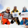 Three climbers in colorful gear sit on a snowy mountain peak, holding signs. The left climber in an orange suit holds a sign reading "Patrasi Peak Expedition 6450M." The middle climber in a yellow and black jacket holds a sign with the Mountain Foundation Seven Summits Treks logo. The right climber in a blue suit holds a sign reading "Access the inaccessible Petzl." Snow-covered mountains and a clear sky are in the background.