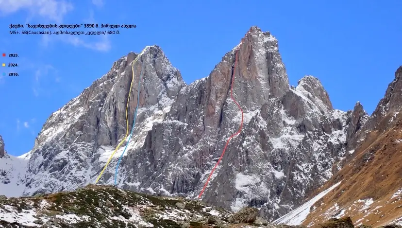 A dramatic view of a jagged, snow-patched alpine peak in the Caucasus Mountains under a clear blue sky. Colored lines (yellow for 2025, red for 2024, blue for 2016) trace different climbing routes up the steep rock face. Georgian text in the top left mentions the peak "Ushba," its elevation of 4690 m (north summit) and 4710 m (south summit), and route grades M5+, 5B (Caucasian), with a difficulty of 680 m.