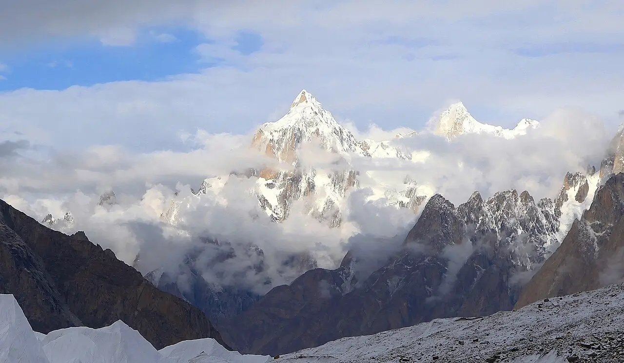 Iconic sharp peak piercing through drifting clouds in the heart of the Karakoram — jagged snow giants and glacier ice below, pure high-altitude wilderness!