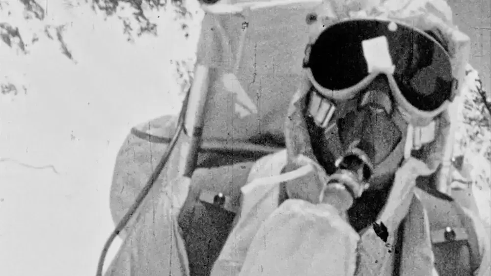 Black-and-white photo of Tom Hornbein on the 1963 Everest West Ridge expedition, wearing oxygen mask, goggles, hooded parka, and heavy backpack with oxygen gear against snowy Himalayan background.