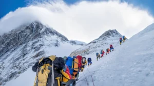 Team of climbers in colorful gear roped up, climbing a snowy mountain slope with peaks in the background