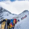 Team of climbers in colorful gear roped up, climbing a snowy mountain slope with peaks in the background