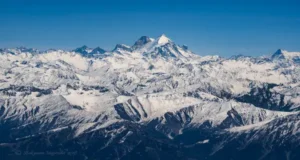 Breathtaking aerial panorama of snow-covered Himalayan mountains in Kashmir: jagged peaks, vast glaciers, and pristine white ridges under a clear bright blue sky.