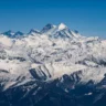 Breathtaking aerial panorama of snow-covered Himalayan mountains in Kashmir: jagged peaks, vast glaciers, and pristine white ridges under a clear bright blue sky.