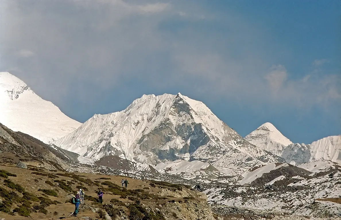 Trekkers hiking toward the dramatic snow-covered peak with clear blue sky above