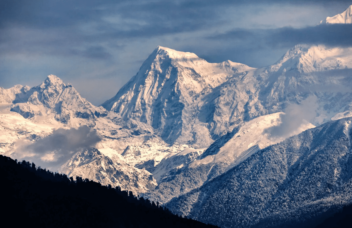 "Stunning snow-covered Himalayan peaks in Nepal at dusk, framed by dark pine forests and dramatic clouds