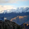 Ancient whitewashed Buddhist stupa or small monastery perched on a rocky hilltop in the Ladakh region, overlooking dramatic snow-capped mountain ranges bathed in warm golden sunset light.